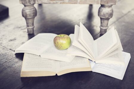 Apple and four open books on a floorの写真素材