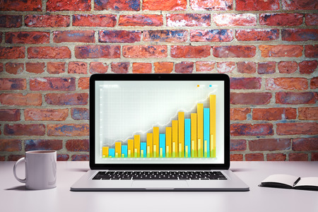 Laptop with business graph on a table with cup of coffee and diaryの写真素材