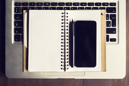 Blank smartphone with blank diary and pen on the keyboard of laptop, mock upの写真素材
