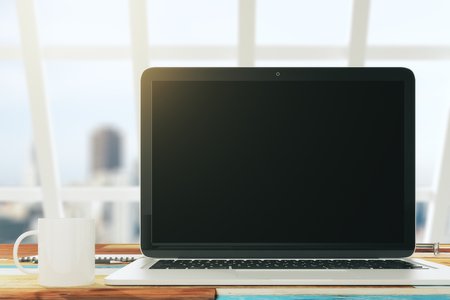 Blank laptop on the desktop in a sunny office with a cup of coffee, mock upの写真素材