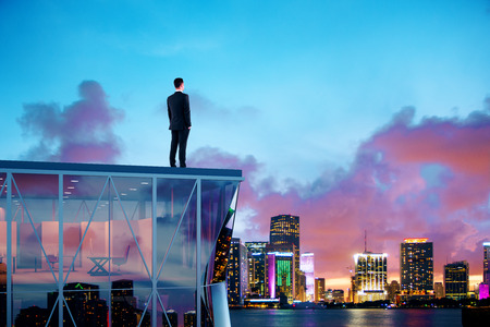 Businessman standing on the roof of a skyscraper and looking over the city at sunriseの写真素材