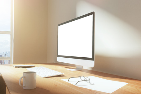Blank screen of monitor with cup of coffee, glasses and keyboard on a wooden table at sunrise, mock upの写真素材