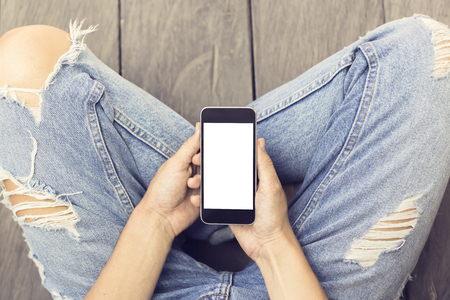 Girl in jeans with blank smartphone on the wooden floor, mock upの写真素材