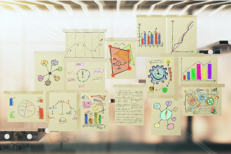 Paper posters with notes and schemes on glassy wall in the office