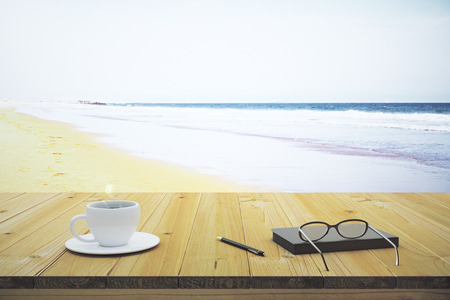 Cup of coffee notebook and glasses on a wooden table on the beachの写真素材