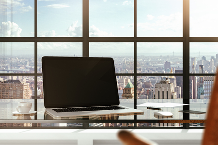 Blank laptop on a glass table in a modern office and city views from the windowsの写真素材