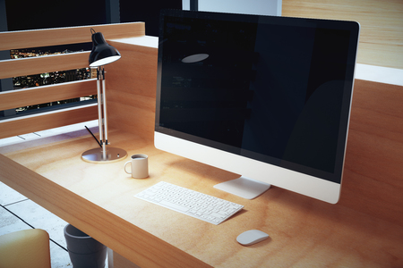 Blank black computer screen on wooden table with lamp and cup of coffee at nightの写真素材