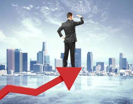 Businessman stays on red arrow from business graph and looking into the distance at city backgroundの写真素材