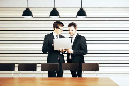 Businessmen with laptop in modern conference room with lamps and furnitureの写真素材