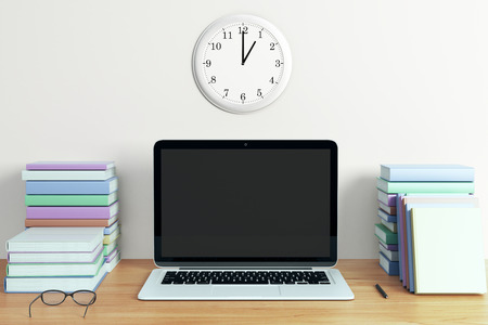 Blank black laptop screen with piles of books on wooden table, mock up
