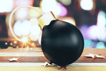 Christmass black small bomb with a lit fuse and golden stars on wooden tableの写真素材