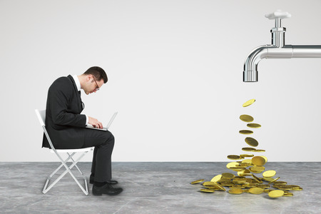 Working businessman with laptop and faucet from which the money flowの写真素材