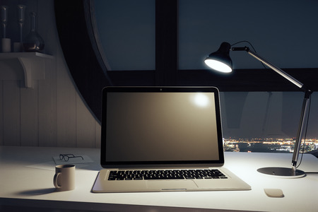 Black blank laptop with cup of coffee and lamp at nightの写真素材