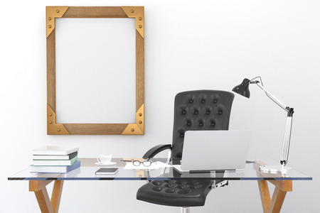 Work desk with a laptop and a blank picture frame on the wall, mock upの写真素材