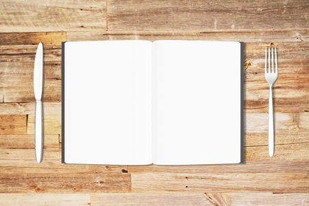 Blank white pages of opened diary with fork and knife on wooden table, mock upの写真素材