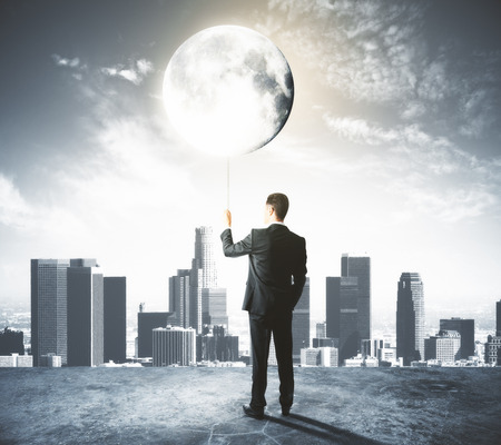 Businessman holds the Moon like a balloon at city backgroundの写真素材