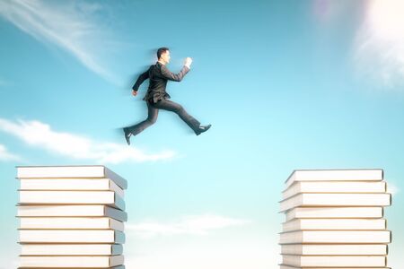 Risk concept with businessman jumping from one book stack onto another in blue skyの写真素材