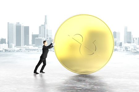 Businessman pushing huge dollar coin on grey city backgroundの写真素材