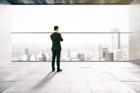 Thoughtful businessman in concrete interior with city view. 3D Renderingの写真素材