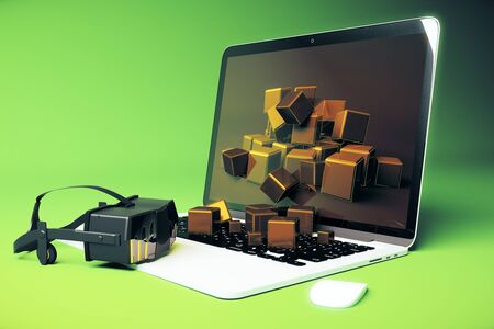 Virtual reality glasses next to laptop with square blocks falling out of screen on green background....