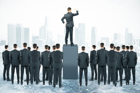 Leadership concept with businessman standing on pedestal and looking into the distance with other businesspeople aroundの写真素材