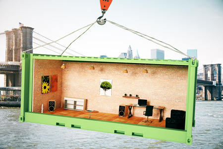 Abstract creative office interior inside green crago container suspended on crane hook on city background. 3D Renderingの写真素材