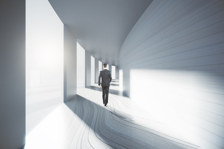 Businessman walking down bright empty corridor interior with sunlight. 3D Renderingの写真素材