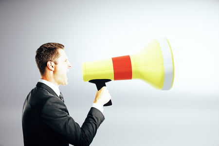 Side view of emotinal businessman screaming into megaphone on grey background. Communication conceptの写真素材