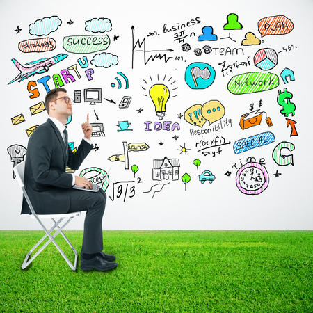 Businessman using laptop and pointing finger up on light background with business drawings. Success conceptの写真素材