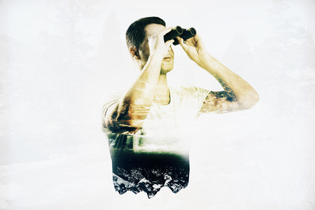 Young man looking binoculars on abstract landscape background. Double exposureの写真素材