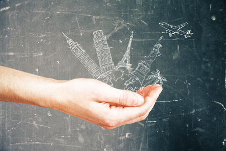 Male hand holding abstract drawing of landmarks and airplane on aged concrete background. Travel conceptの写真素材