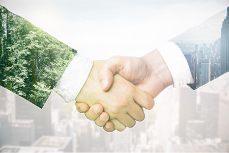 Closeup of businesspeople's handshake on abstract light background with city and forest. Double exposure. Business conceptの写真素材