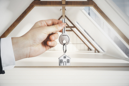 Hand holding key with house keychain on loft interior background. Real estate and mortgage conceptの写真素材