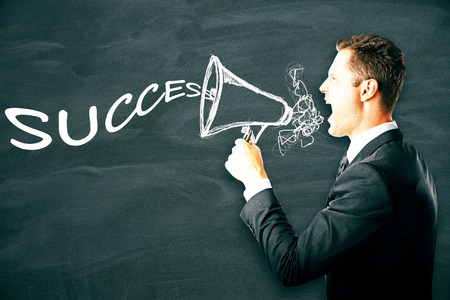 Emotional businessman screaming into abstract drawn megaphone with text on chalkboard background. Success conceptの写真素材
