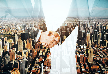 Businessmen shaking hands on city background. Partnership concept. Double exposureの写真素材