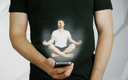 Close up of casual man holding smartphone with abstract meditating person hologram. Peace conceptの写真素材