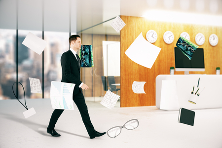 Businessman walking in blurry office interior with city view and abstract flying objects. 3D Renderingの写真素材