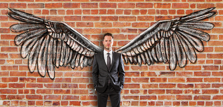 Young businessman in suit with creative drawn wings on red brick wall backgroundの写真素材