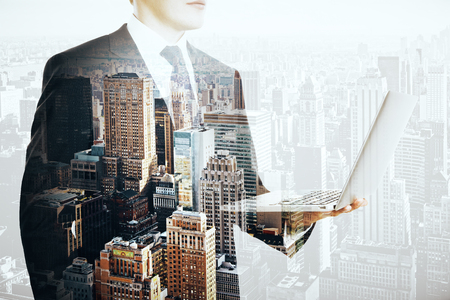 Side view of young businessman using notebook on abstract city background. Double exposureの写真素材