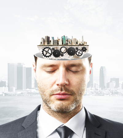 Portrait of handsome caucasian businessman with closed eyes and abstract cogwheels inside head on city background.の写真素材