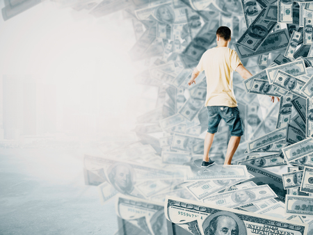 back view of young man surfing dollar banknote wave. Bright background. Success and wealth conceptの写真素材