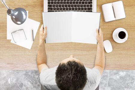 Top view of young businessman at office desktop holding empty open book. Mock up, 3D Renderingの写真素材