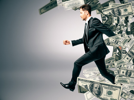 Running businessman with dollar banknote wave ob grey background. Success and wealth conceptの写真素材