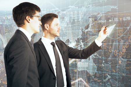 Two handsome businessmen writing something on abstract city and forex chart background. Fund management concept. Double exposureの写真素材