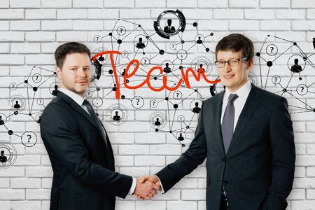 Handsome cheerful caucasian businessmen shaking hands on brick background with creative polygonal pattern. Team conceptの写真素材