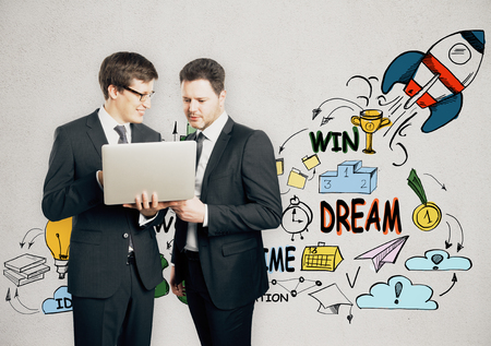 Young european businessmen using laptop with abstract business sketch on concrete wall background. Teamwork conceptの写真素材