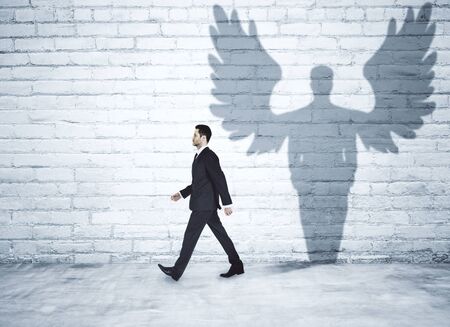 Walking businessman with angel shadow in brick interiorの写真素材