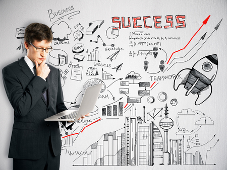 Young european businessman using laptop with abstract business sketch on concrete wall background. Entrepreneurship conceptの写真素材