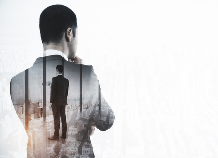 Back view of thoughtful young businessman in interior with city view and copy space. Career concept. Double exposureの写真素材