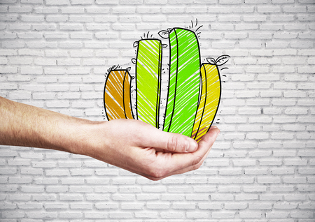 Side view of businessman's hand holding green business chart on brick background. Financial growth conceptの写真素材